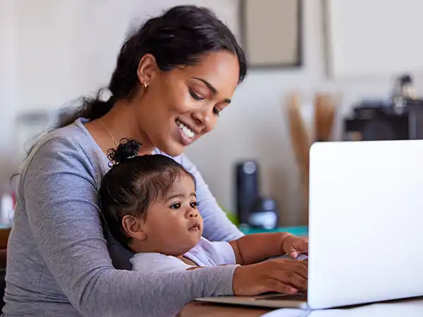 A woman working at home on her laptop with her young child in her lap