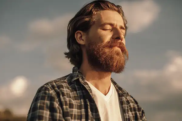 A bearded man outside feeling the rays of the sun