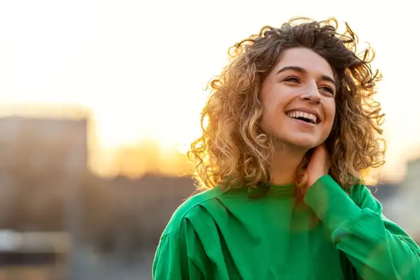 A young woman smiling while the sun sets behind her.