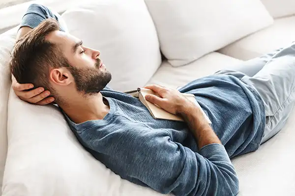 A man who has fallen asleep on a couch with a book