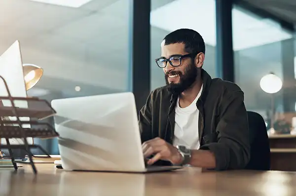 A man wearing glasses smiling at his computer