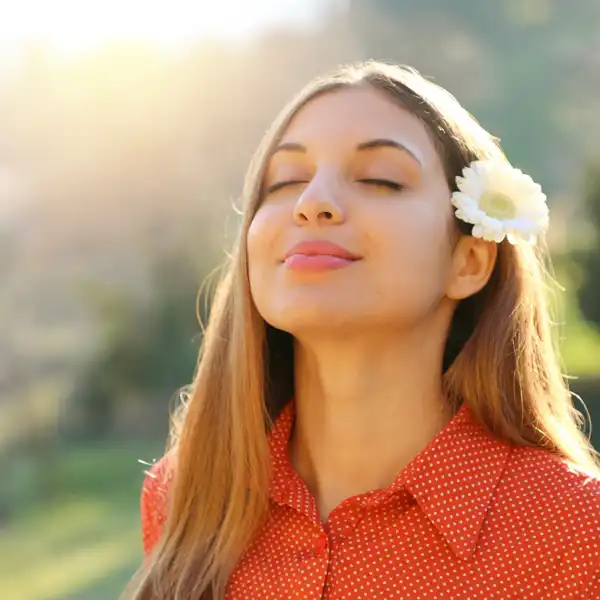 A woman with a flower in her hair feeling the rays of sunlight outside
