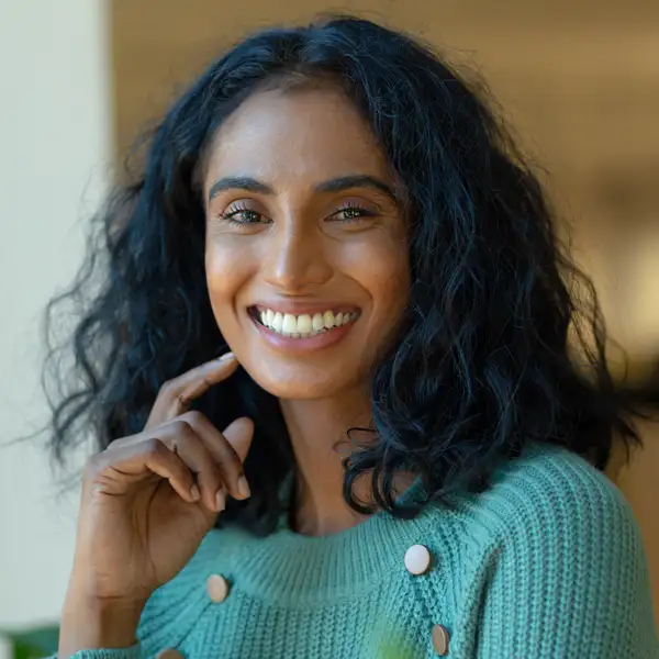 A woman in a blue shirt smiling and pointing towards her teeth