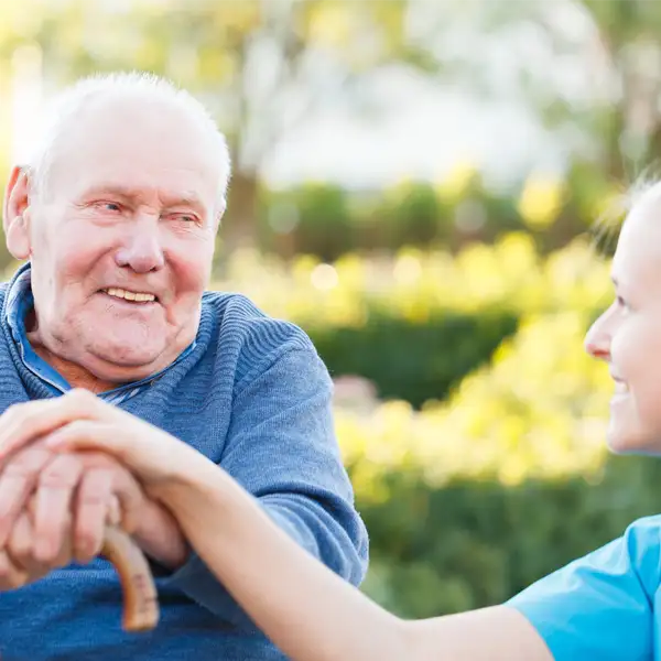 A young person holding hands with an older man on top of his cane while sitting at a bench