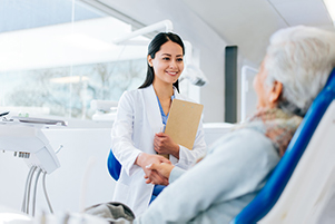 A dentist meeting an older female patient in the dental chair.